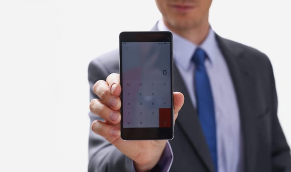 A businessman holding smartphone in hand demonstrates display on which calculator is depicted with figure of zero. The accountant has calculated all transactions are correct debt has credit approx ok