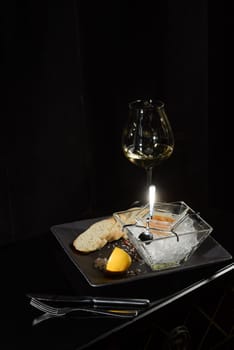 Pike fish caviar, on ice, with croutons and butter, on a transparent dish with a glass of white wine on a dark background