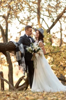 beautiful happy stylish bride in hat and groom standing outdoor in autumn