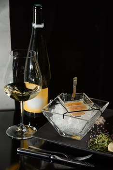 Pike fish caviar, on ice, with croutons and butter, on a transparent dish with a glass of white wine on a dark background