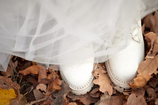 bride wearing white boots and white dress is standing on fall leaves. autumn wedding