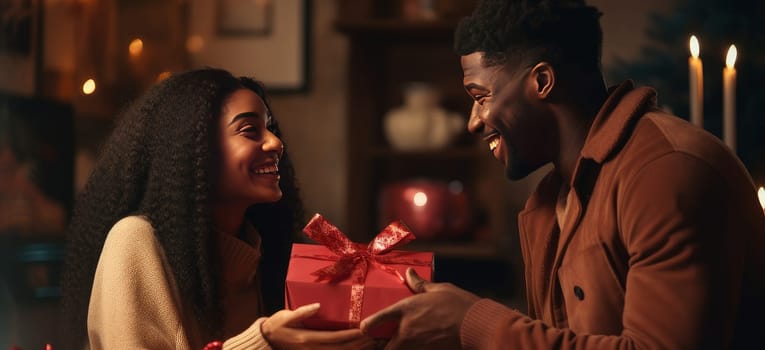 A young African-American black couple in love, a man and a woman. A chic, happy man gives a gift in a box to a beautiful smiling woman, with care and love. Valentine's day, newlyweds, engagement holiday, birthday, wedding, anniversary, surprise, date