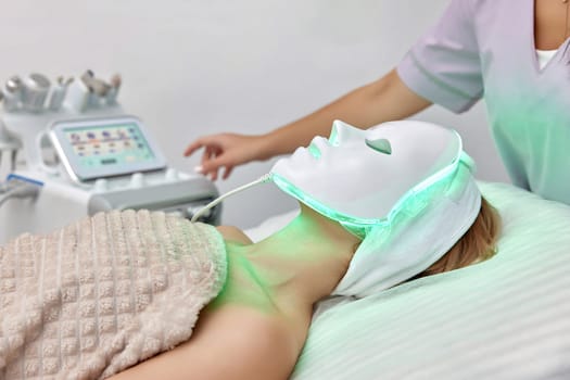 woman getting cosmetic procedure with LED facial mask in beauty salon