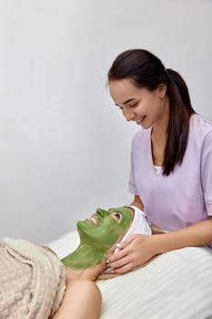female beautician applies the mask to the face of beautiful woman in the spa salon. facial skin care