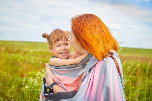 Happy female family with mother and daughter on green and yellow meadow full of grass and flower. Woman with red hair and blonde girl having fun, joy and hug in sunny summer day. Concept family love