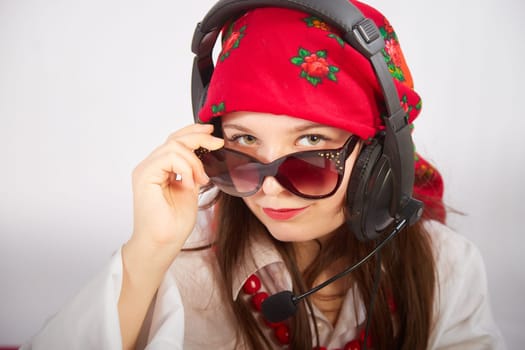 Portrait of young girl in red scarf, large headphones with microphone and black glasses. Woman who is radio or television presenter in workplace. Funny female telecom operator. Freelancer at work