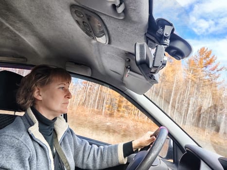 Portrait of female driver in solo journey. Adult mature woman holding steering wheel and looking through windscreen in travel by vehicle on vacation. Lady girl who is owner or rent car for travel