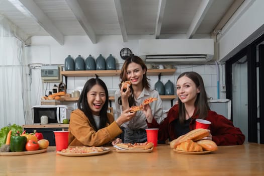 A group of young female friends have a party with pizza on the table and red drink glasses. Talk and live together happy, having fun at home..