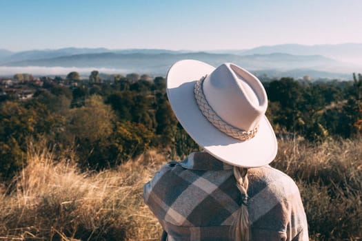 A woman stands in a meadow and looks at the mountains.