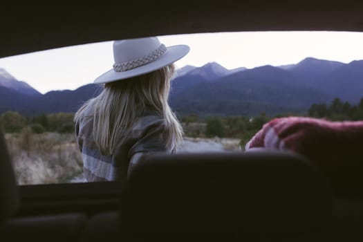 Woman traveler sitting on hatchback car with mountain background