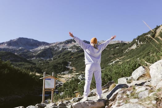 Young female traveler stands alone with arms outstretched on a mountain path enjoying the view