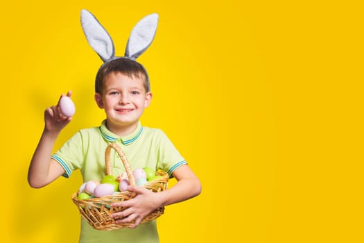 Cute little child is wearing bunny ears on Easter day and holding basket with painted eggs. Happy kid is holding Easter basket.