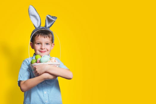 Cute little child is wearing bunny ears on Easter day and holding basket with painted eggs. Happy kid is holding Easter basket.
