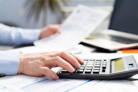 Man with bills and calculator. Businessman using calculator to calculate bills at the table in office. Financial accounting concept.
