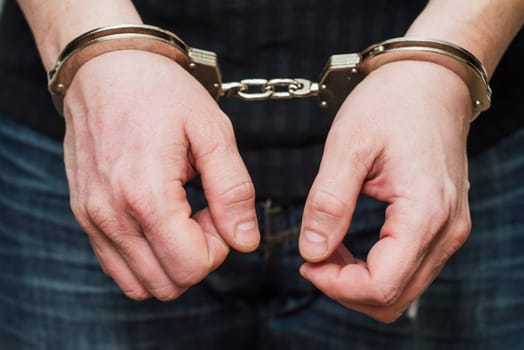 Man detained in handcuffs. Prisoner or arrested man in handcuffs. Male hands in handcuffs. Criminal law.
