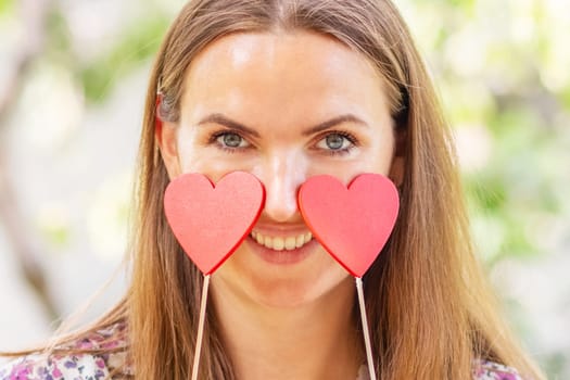 Happy beautiful woman with two decorative hearts in her hands is smiling on the natural backround.