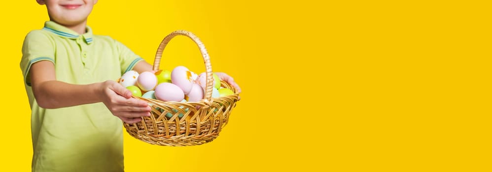Little child is holding basket with painted eggs on yellow background. Easter day.