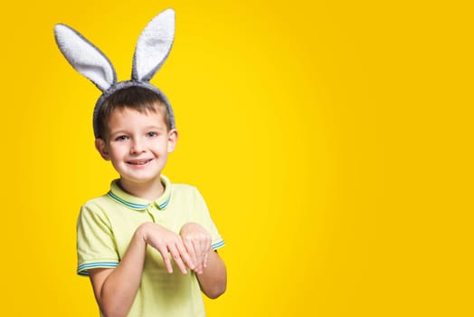 Portrait of a smiling adorable little boy wearing bunny ears on a yellow background.