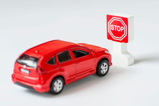 A car and stop road sign on a white background. Toy car parked next to a toy stop sign. Traffic Laws.