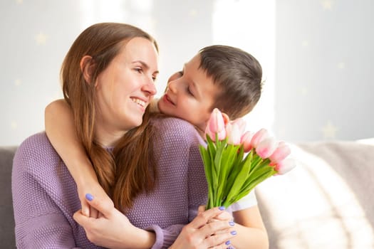 A cute son giving his mother a bouquet of tulips congratulating her on mother's day while celebrating the holiday at home.