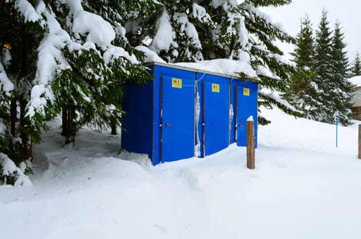 Snow-covered, blue, portable toilet on a winter day