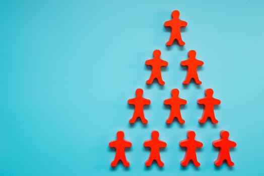 Team of toy people are showing concept of teamwork. Pyramid of red toy people on blue background. Business concept.