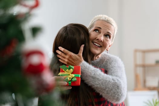 Thankful Caucasian woman with christmas gift hugging daughter at home.