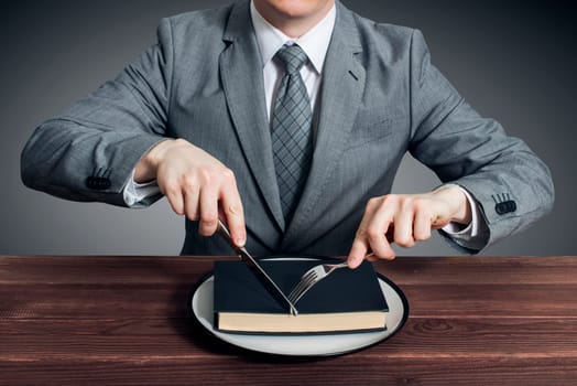 A businessman with a fork and knife eats a book on a plate. The concept of education, professional development