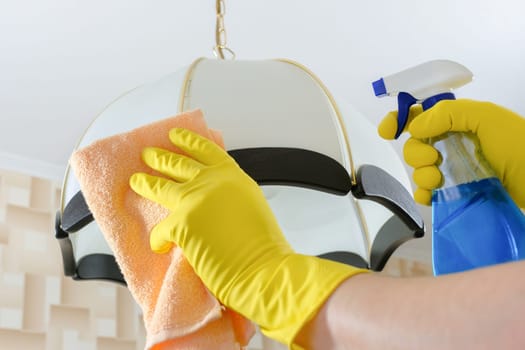 The cleaner wipes the dust from the chandelier with a rag and detergent. Cleaning service.