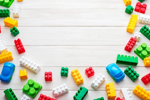 Top view of colorful plastic toy bricks on a white wooden background. Baby kids toys background.