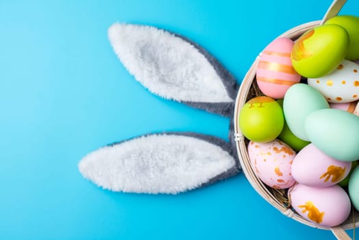 A basket of Easter eggs with bunny ears on blue background. Top view. Easter greeting card.
