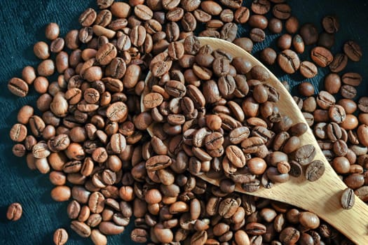 Background of roasted coffee beans and wooden scoop close up. View from above.