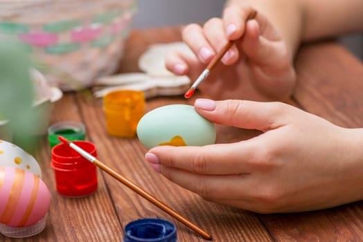 A woman with a tassel paints Easter eggs. Preparing decorations for Easter, creativity with children, traditional symbols. Preparing for Easter.