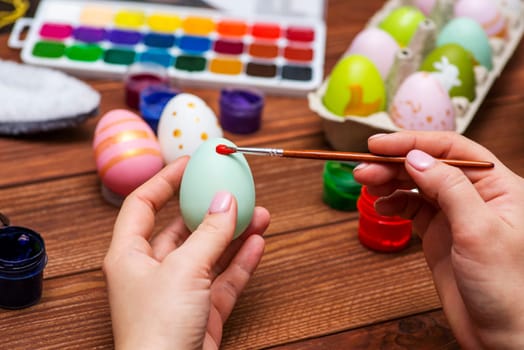 A woman with a tassel paints Easter eggs. Preparing decorations for Easter, creativity with children, traditional symbols. Preparing for Easter.