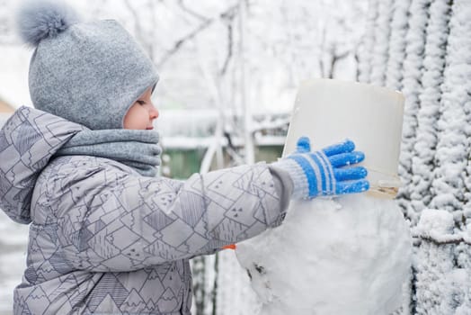 Cute little boy is making a snowman. Child playing with snow. Children wintertime outdoor activitie time concept.