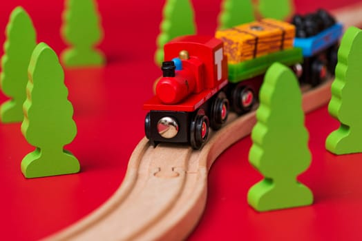 Wooden toy train on the railroad among green trees on red background. Educational toys for preschool and kindergarten child.