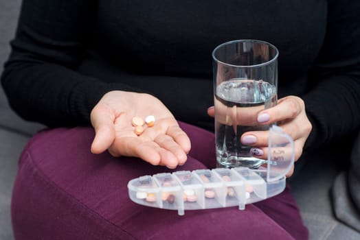 Woman holds tablet and glass of water. Female going to take tablet from headache or painkiller or abortion pill medication drinking clear water from glass.