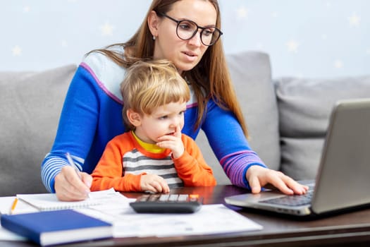 Business woman is working at home on a laptop with her baby. Concept of female business, working mom, freelancing, home office. Lifestyle moment.