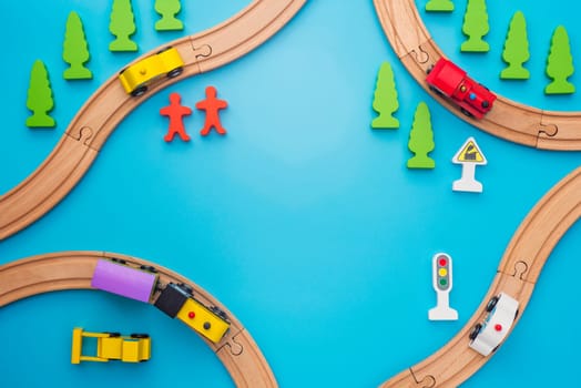 Baby kid toys background. Toy train and wooden rails on blue background. Top view. Children toys, a trains and cars traveling on wooden roads with trees, people and roadsigns on blue background.