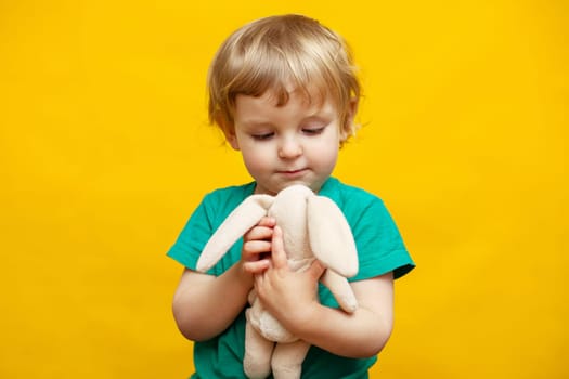 Cute little kid hugging a plush rabbit bunny toy on yellow background. Concept of childhood. Toy and child.