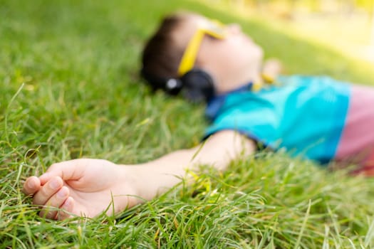Happy boy in sunglasses lying on the grass and listening to music in headphones on a sunny day.
