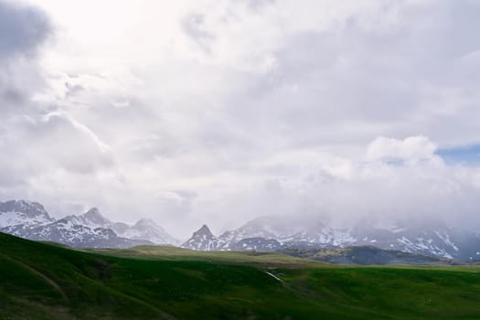 Fog over snow-capped mountains descends onto a green valley. High quality photo