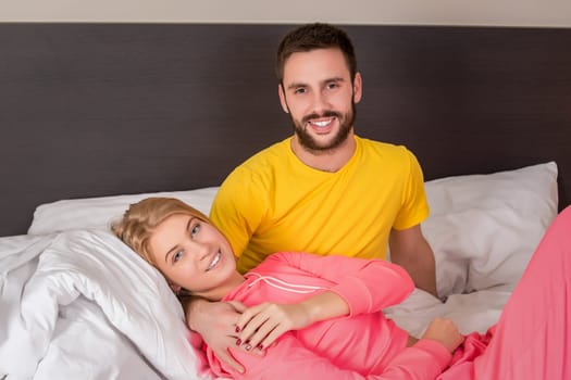 Young lovely couple lying and have fun in a bed, happy smile looking at camera. Family, bedtime and happiness concept