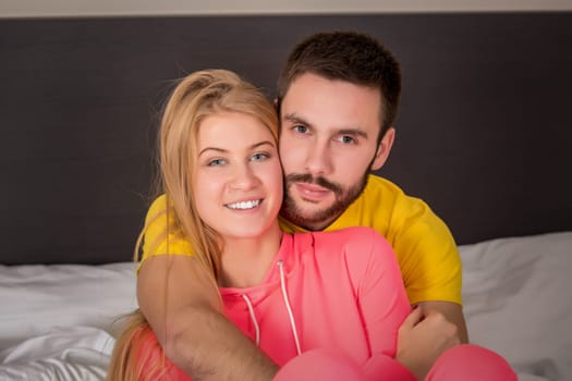 Young lovely couple lying and have fun in a bed, happy smile looking at camera, closeup. Family, bedtime and happiness concept