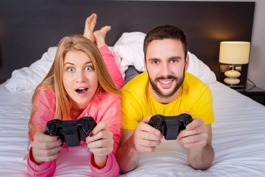 Happy young couple having fun playing videogames in bed.