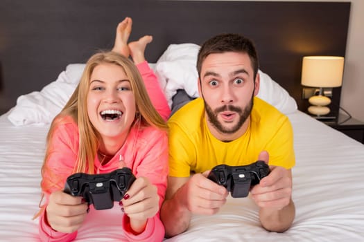 Happy young couple having fun playing videogames in bed.