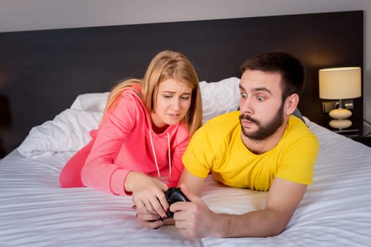 Young couple having playing videogames in bed. Guy playing a video game, she complains that she did not pay attention