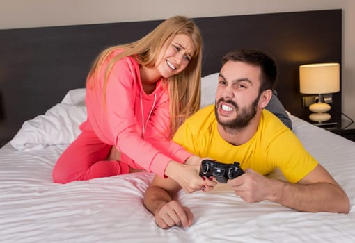 Young couple having playing videogames in bed. Guy playing a video game, she complains that she did not pay attention