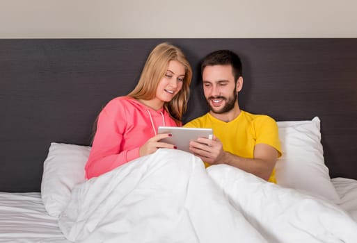 Young Sweet Couple on Bed Watching Something on Tablet Gadget. Concept about technology and people