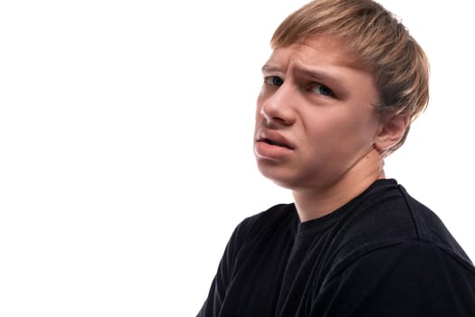 Upset fair-haired teenager guy in a black T-shirt on a white background.